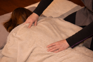 Séance de shiatsu bien-être dans la Marne, mains posées avec douceur sur le dos, favorisant le relâchement et la détente profonde.